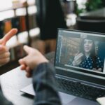 Crop anonymous woman teaching sign language to female student during video call via laptop in light workspace